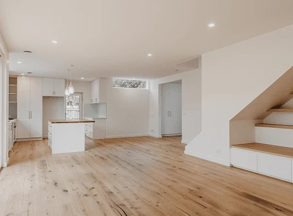 Modern open-plan kitchen and living area with natural oak flooring, white cabinetry, built-in storage under stairs, and minimalist design in a new residential home.