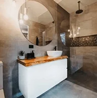 Croydon Modern bathroom design featuring a large round mirror, pendant lighting, a vessel sink on a wooden countertop, and textured wall tiles – Coy’s Constructions renovation project.