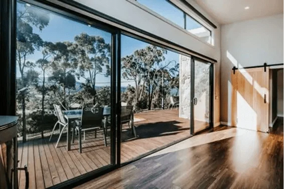 Contemporary living room with expansive glass sliding doors opening to a timber deck overlooking bushland, built by Coy’s Constructions in the Yarra Ranges.