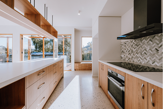 Poet s Cottage House 05 600x400 1 | Coy's Constructions Contemporary kitchen interior with wood cabinetry, white countertops, herringbone tile backsplash, and built-in modern appliances – natural light from large windows enhances the space.